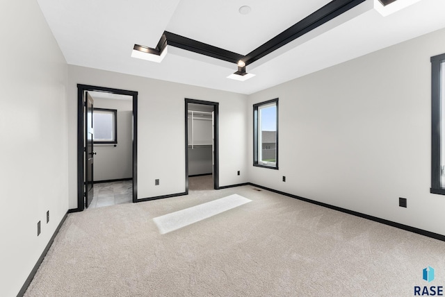 unfurnished bedroom with a closet, a spacious closet, light colored carpet, and a raised ceiling