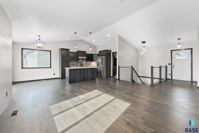 kitchen with hanging light fixtures, dark wood-type flooring, stainless steel appliances, and a center island with sink