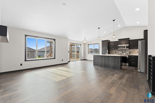 kitchen with appliances with stainless steel finishes, decorative light fixtures, an island with sink, backsplash, and dark hardwood / wood-style flooring