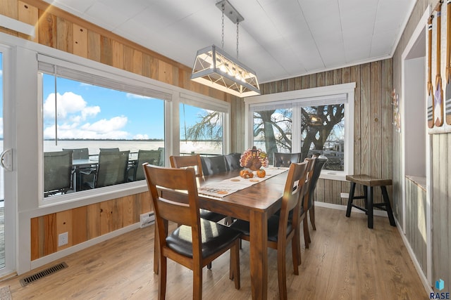 dining area with crown molding, a water view, hardwood / wood-style floors, and wood walls