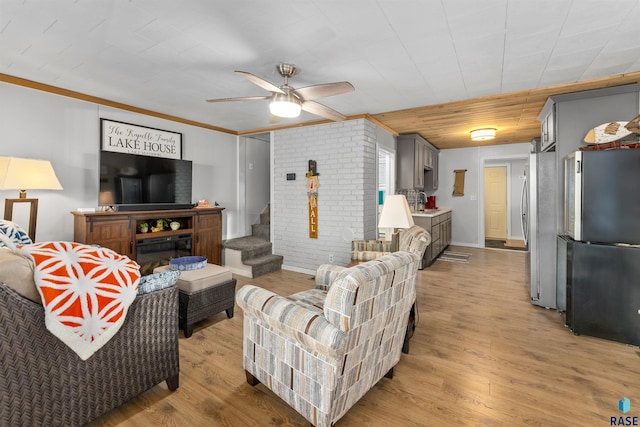 living room with ceiling fan, brick wall, crown molding, and light wood-type flooring