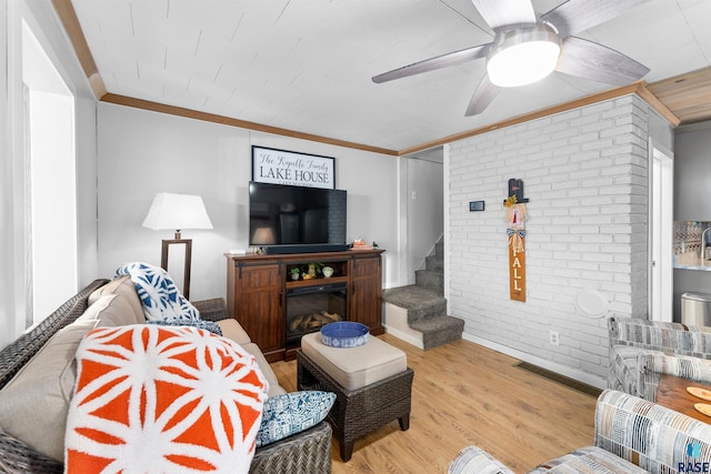 living room with light hardwood / wood-style flooring, ornamental molding, and brick wall