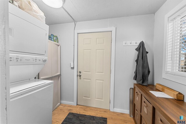 laundry area with stacked washing maching and dryer and light hardwood / wood-style flooring