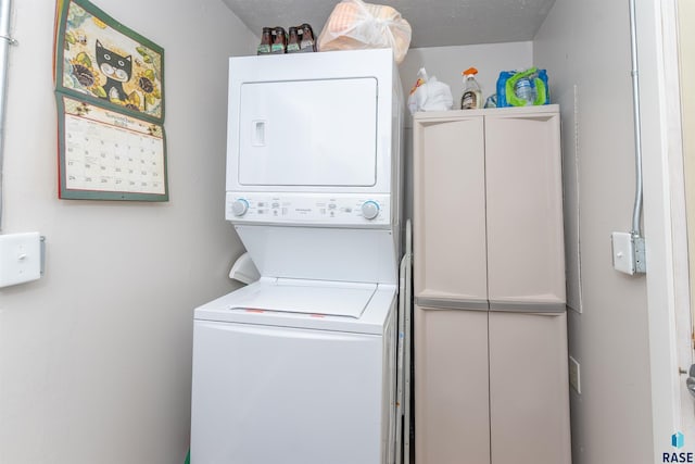 laundry area featuring cabinets, stacked washer / drying machine, and a textured ceiling