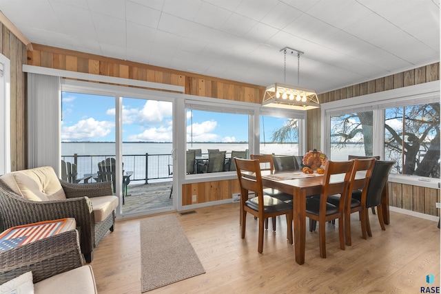 dining space with light wood-type flooring, wood walls, and a water view