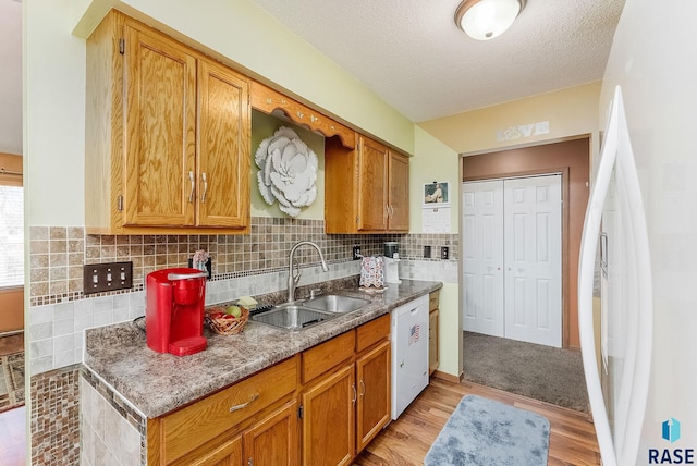 kitchen featuring tasteful backsplash, sink, white appliances, light hardwood / wood-style floors, and a textured ceiling