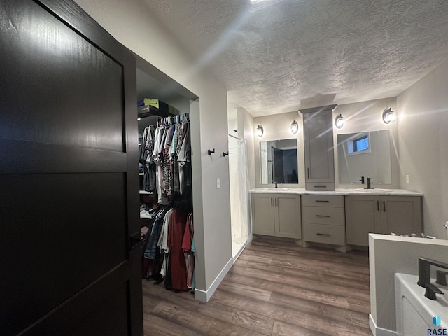 full bathroom with a spacious closet, vanity, a textured ceiling, wood finished floors, and baseboards