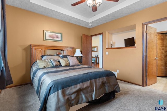 carpeted bedroom featuring ceiling fan, a tray ceiling, and a textured ceiling