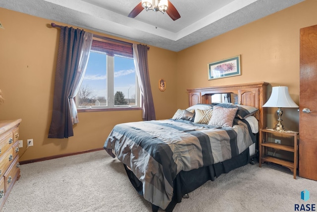 carpeted bedroom with ceiling fan, a tray ceiling, and a textured ceiling