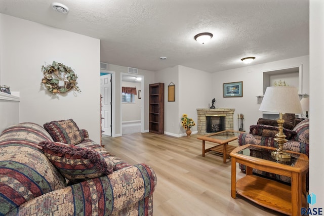 living room featuring a stone fireplace, a textured ceiling, and light hardwood / wood-style floors