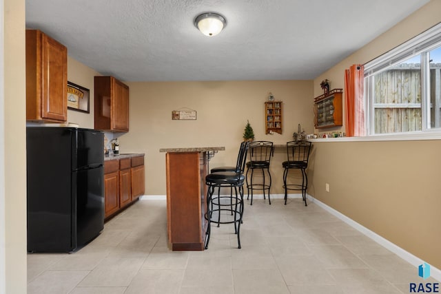 kitchen featuring black refrigerator, a breakfast bar area, a textured ceiling, and kitchen peninsula