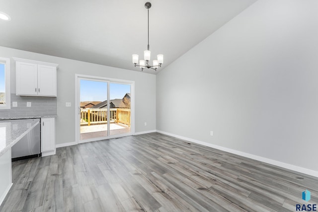 unfurnished dining area with vaulted ceiling, a notable chandelier, and light hardwood / wood-style floors