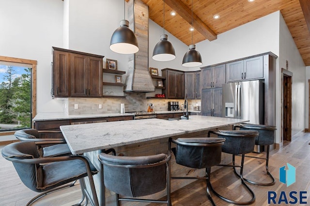 kitchen featuring pendant lighting, an island with sink, dark brown cabinetry, light stone counters, and wood ceiling