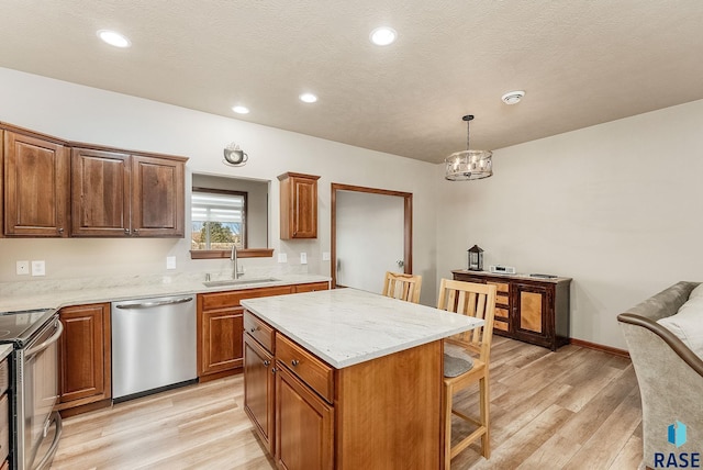 kitchen with sink, appliances with stainless steel finishes, a center island, light hardwood / wood-style floors, and decorative light fixtures