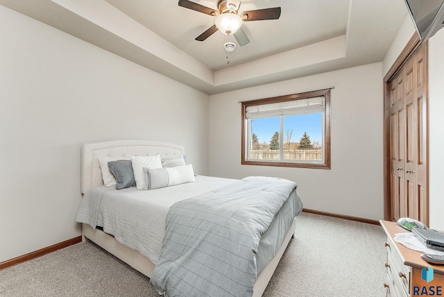 bedroom featuring a tray ceiling, light colored carpet, a closet, and ceiling fan