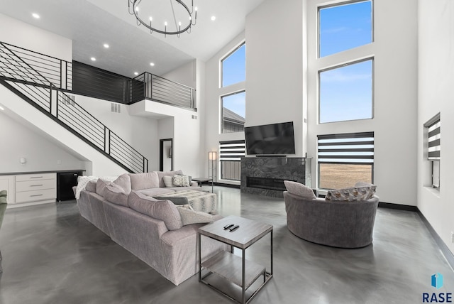 living room with a premium fireplace, a towering ceiling, concrete floors, and an inviting chandelier