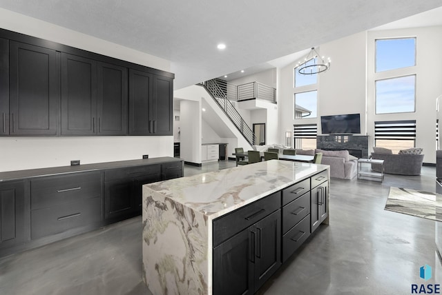 kitchen with a notable chandelier, a center island, concrete floors, and light stone counters