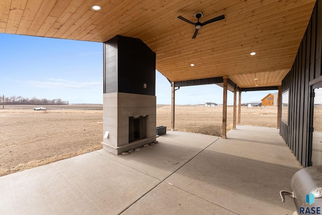 view of patio with a large fireplace, a rural view, and ceiling fan