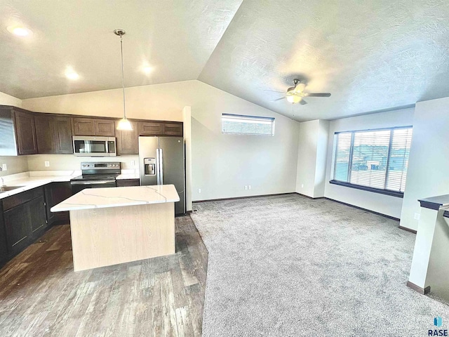 kitchen with appliances with stainless steel finishes, pendant lighting, a center island, light stone countertops, and dark brown cabinets