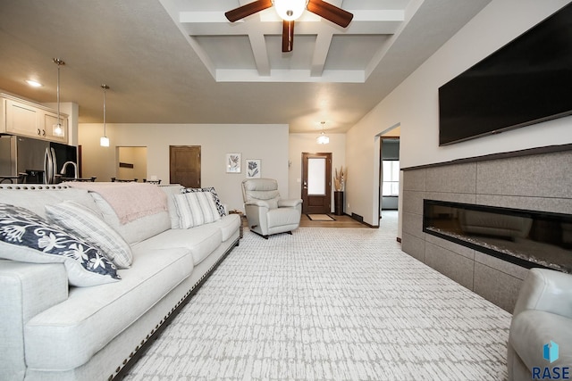 living room featuring a fireplace, beamed ceiling, coffered ceiling, light colored carpet, and ceiling fan