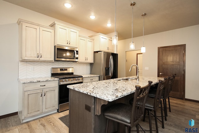 kitchen featuring sink, appliances with stainless steel finishes, a kitchen island with sink, light stone countertops, and decorative light fixtures