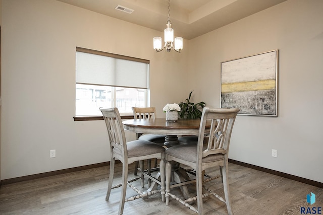 dining space featuring wood-type flooring, an inviting chandelier, and a tray ceiling