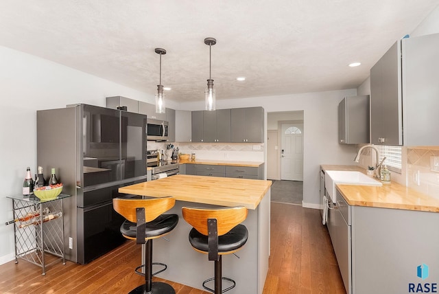 kitchen featuring sink, gray cabinets, appliances with stainless steel finishes, backsplash, and wood-type flooring