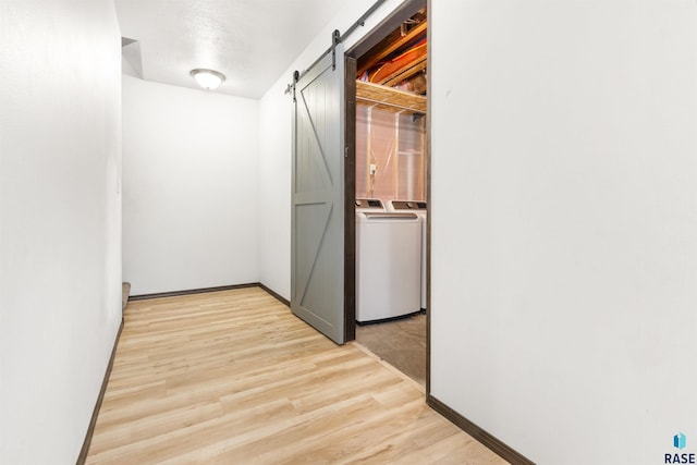 hallway featuring independent washer and dryer, a barn door, and light hardwood / wood-style flooring