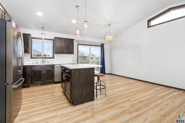 kitchen with a kitchen bar, sink, hanging light fixtures, appliances with stainless steel finishes, and a kitchen island