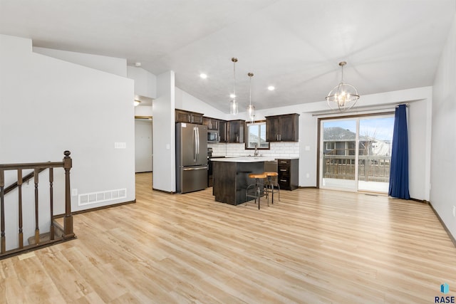 kitchen featuring lofted ceiling, a breakfast bar area, decorative light fixtures, appliances with stainless steel finishes, and a kitchen island