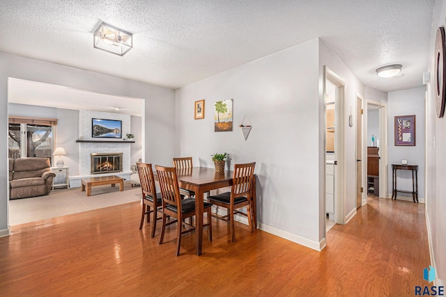 dining room featuring wood-type flooring, a textured ceiling, and a fireplace