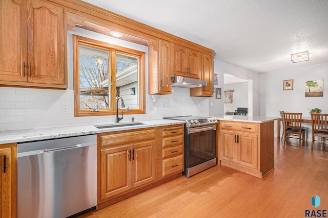 kitchen featuring sink, light stone counters, kitchen peninsula, stainless steel appliances, and light hardwood / wood-style flooring