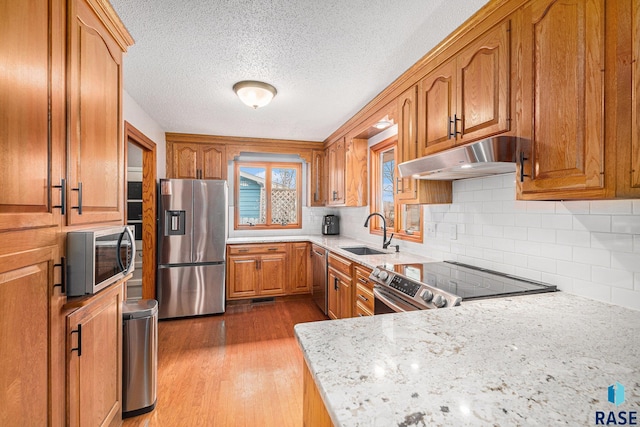 kitchen with sink, light stone counters, stainless steel appliances, light hardwood / wood-style floors, and backsplash