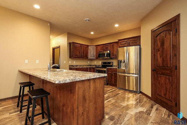 kitchen featuring a kitchen bar, sink, light stone counters, appliances with stainless steel finishes, and kitchen peninsula