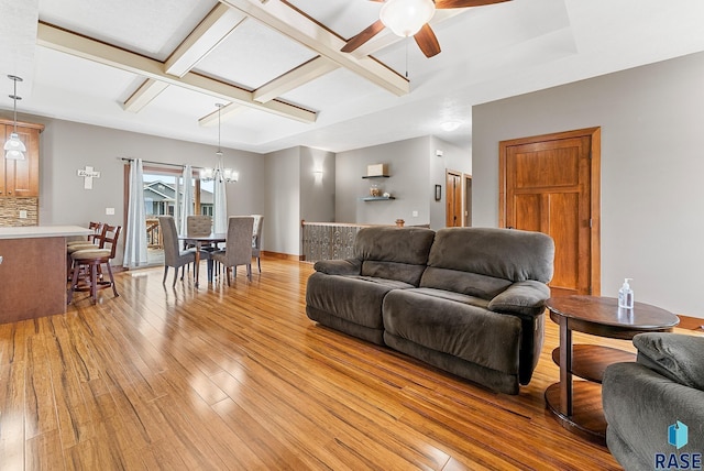 living room with coffered ceiling, ceiling fan with notable chandelier, a raised ceiling, beamed ceiling, and light wood-type flooring