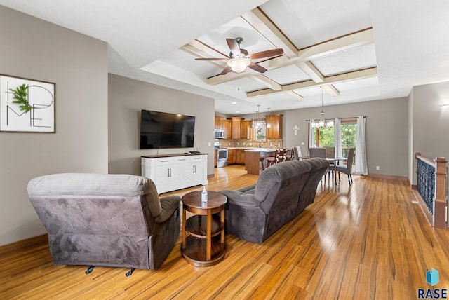 living room with beam ceiling, coffered ceiling, ceiling fan with notable chandelier, and light wood-type flooring