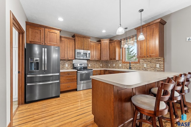 kitchen with a breakfast bar area, appliances with stainless steel finishes, hanging light fixtures, backsplash, and kitchen peninsula