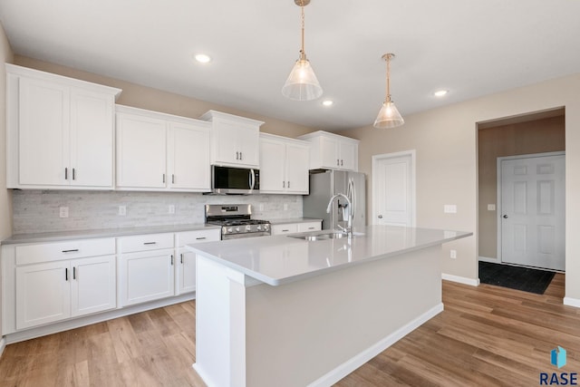 kitchen with a kitchen island with sink, stainless steel appliances, a sink, white cabinets, and light wood-style floors