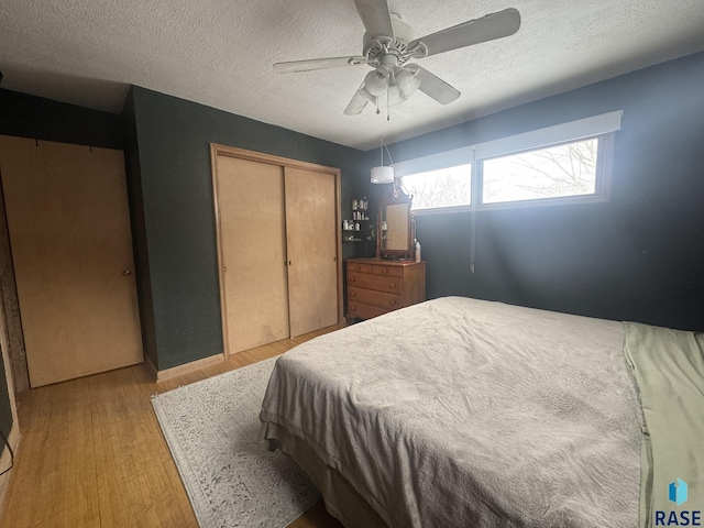 bedroom with light wood-style flooring, a textured ceiling, ceiling fan, and a closet