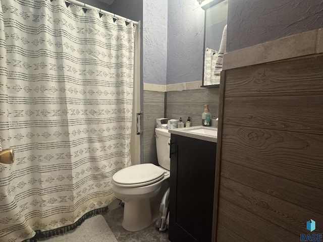 bathroom with wainscoting, toilet, a textured wall, vanity, and tile walls