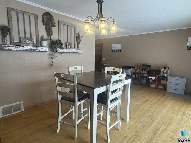 dining room with light wood finished floors, visible vents, an inviting chandelier, and ornamental molding