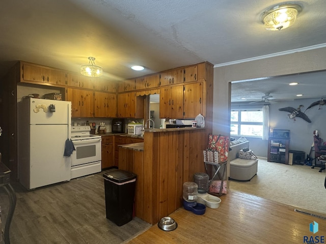 kitchen with brown cabinets, dark countertops, dark wood-type flooring, white appliances, and a peninsula