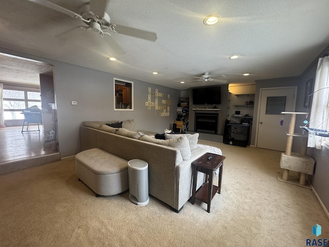 living area featuring a textured ceiling, a fireplace, a ceiling fan, and light colored carpet