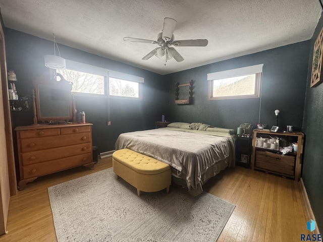 bedroom featuring a ceiling fan, multiple windows, a textured ceiling, and wood finished floors