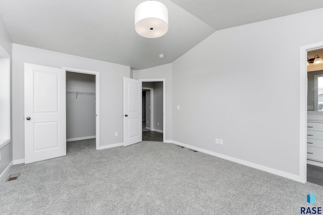 unfurnished bedroom featuring vaulted ceiling, carpet floors, ensuite bathroom, and a closet