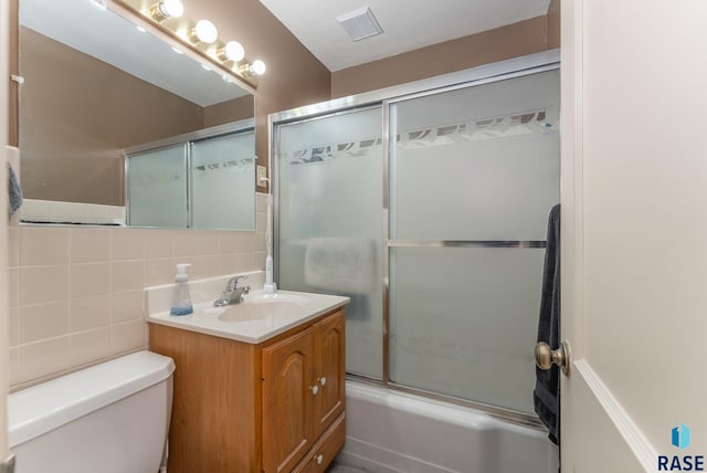 full bathroom featuring vanity, toilet, combined bath / shower with glass door, and tile walls