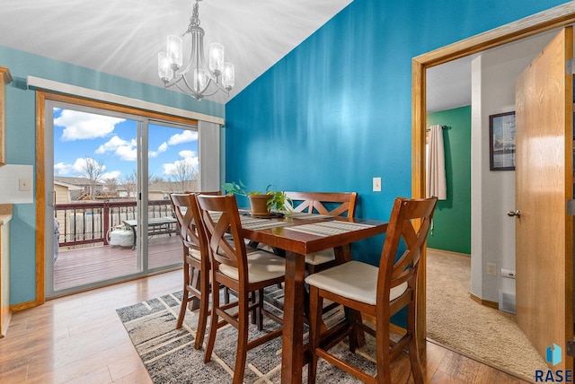 dining space featuring hardwood / wood-style flooring, vaulted ceiling, and a notable chandelier