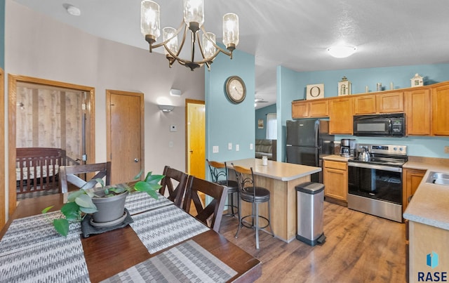 kitchen featuring a breakfast bar area, decorative light fixtures, vaulted ceiling, light wood-type flooring, and black appliances