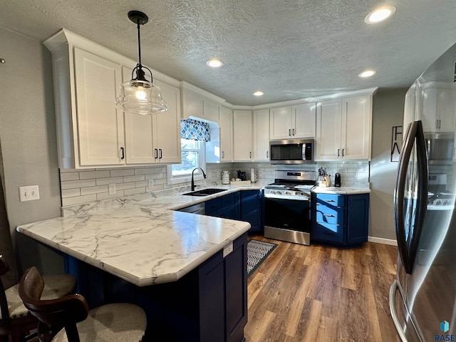 kitchen with sink, white cabinetry, decorative light fixtures, appliances with stainless steel finishes, and kitchen peninsula