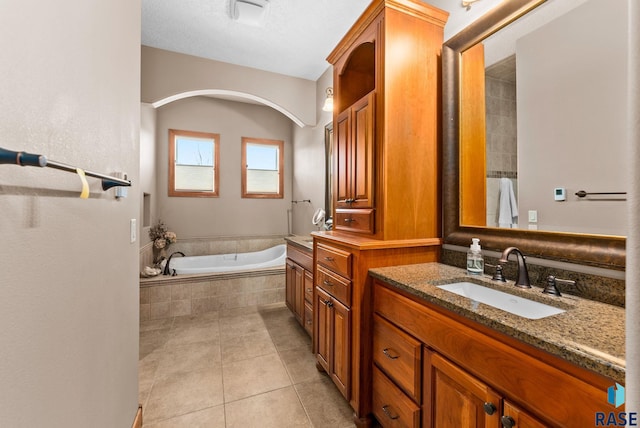 bathroom with a relaxing tiled tub, vanity, and tile patterned flooring